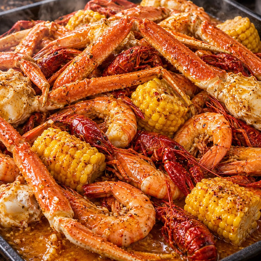 A close-up of a seafood boil or crawfish and shrimp pot with lobster legs, shrimp, corn on the cob, and red crawfish in a glossy orange-brown broth.