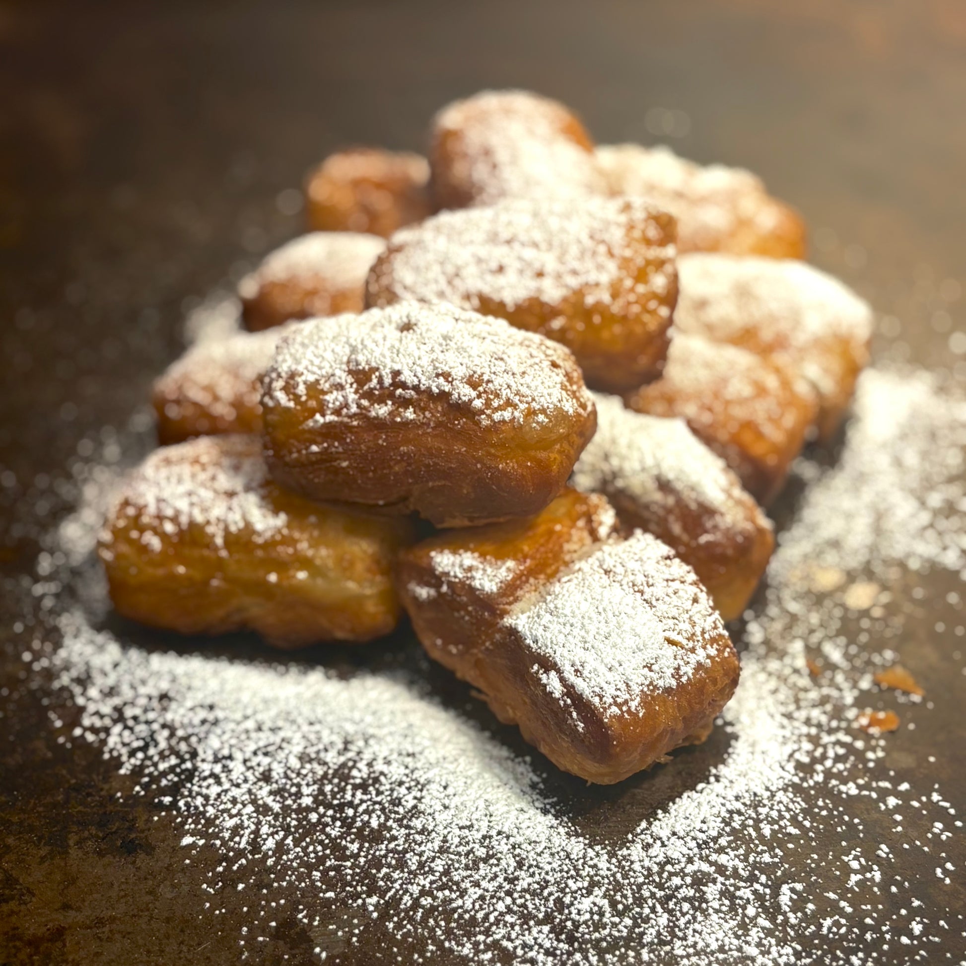 Pastry items dusted with powdered sugar on a dark surface, specifically beignets from New Orleans in West Hollywood. 