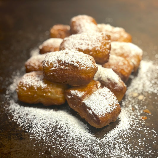 Pastry items dusted with powdered sugar on a dark surface, specifically beignets from New Orleans in West Hollywood. 