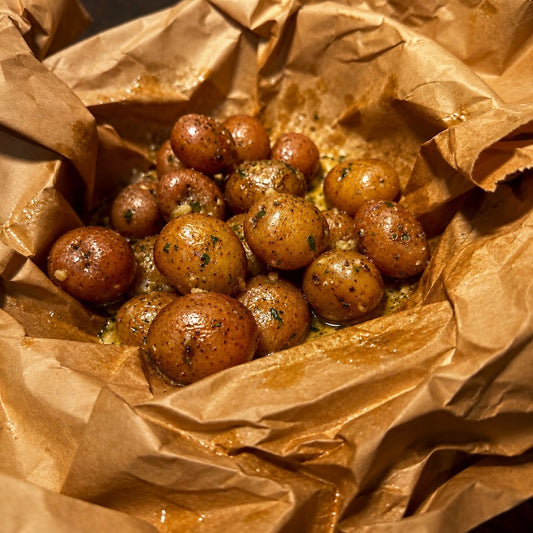 Roasted baby potatoes seasoned with herbs and spices, nestled inside a crumpled brown parchment paper bag.