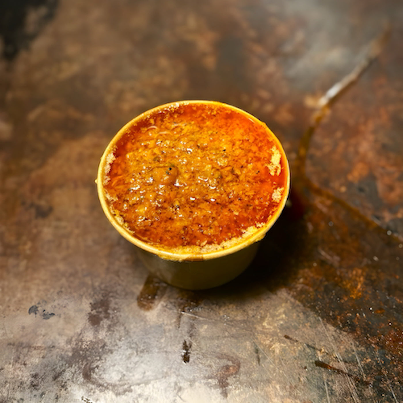 Close-up of a Cajun butter sauce cup with aromatic orange-red spice blend on top — Boil Baby Boil signature dipping sauce for seafood boils