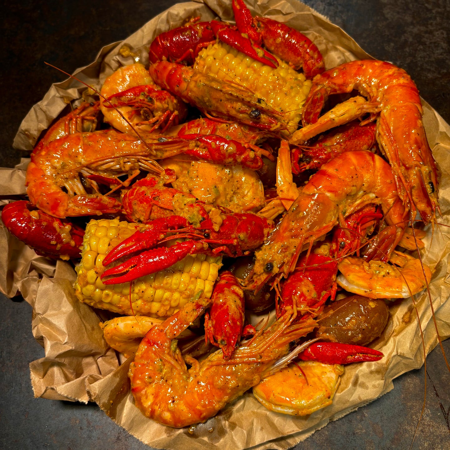 Assorted seafood including shrimp, crawfish, and corn on a paper-lined plate.