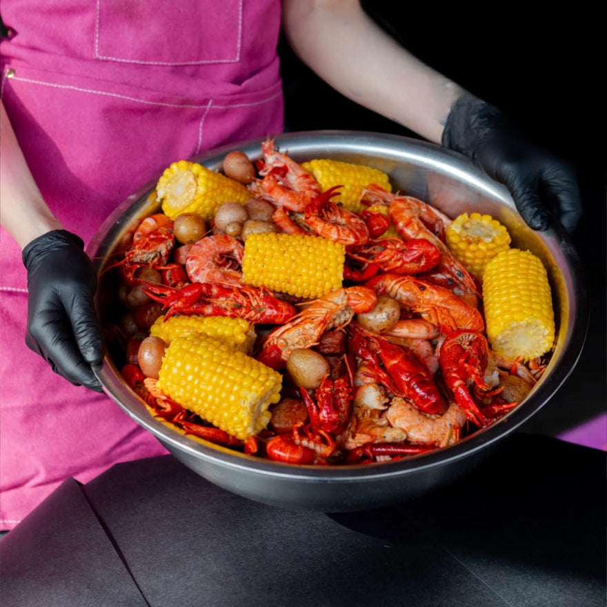 Person holding a large metal bowl filled with crawfish, corn, and other seafood.