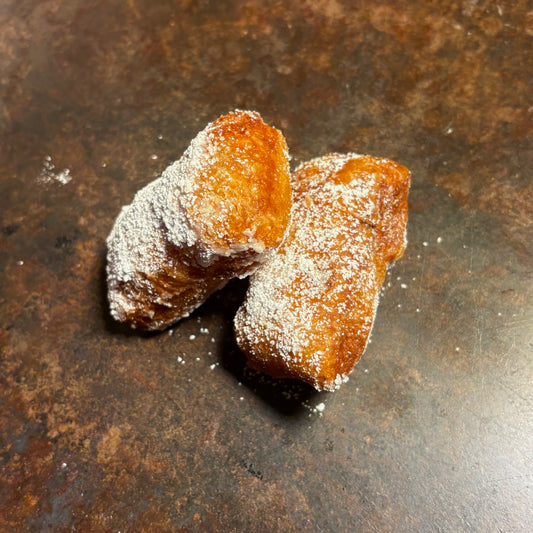 Two fried pastries look to be classic. Beignets straight from New Orleans dusted with powdered sugar on a rusty metal surface