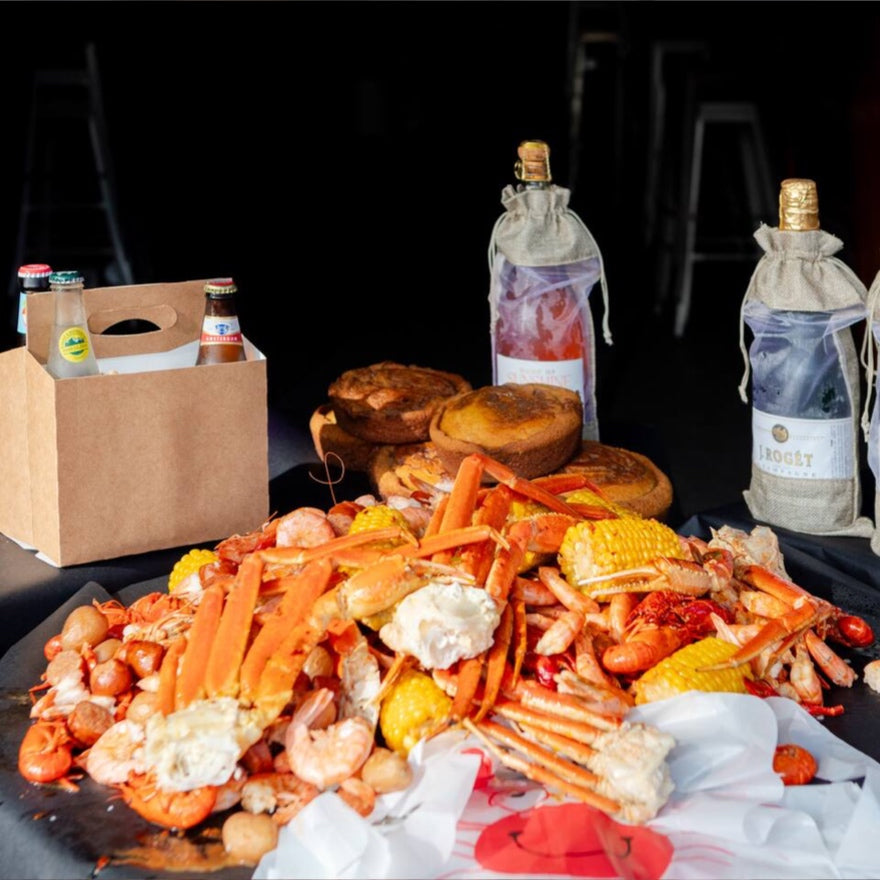 Cajun seafood boil platter with sauces, drinks, and Drip Kit box on dark background in Los Angeles