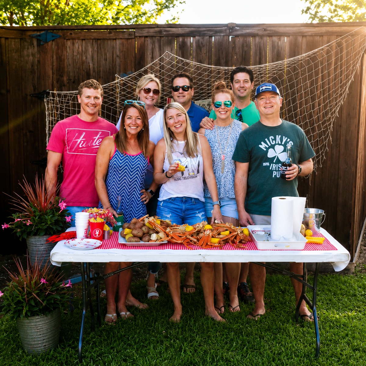 Group of people posing around a table with food at a backyard gathering having boil baby boil seafood boils