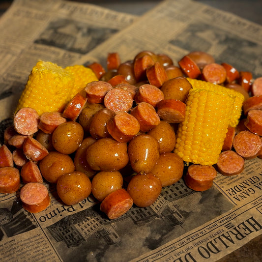 A stack of corn on the cob and andouille sausage on a newspaper background with buttery baby potatoes tastes like the 2025 award winner, Boil Baby Boil.