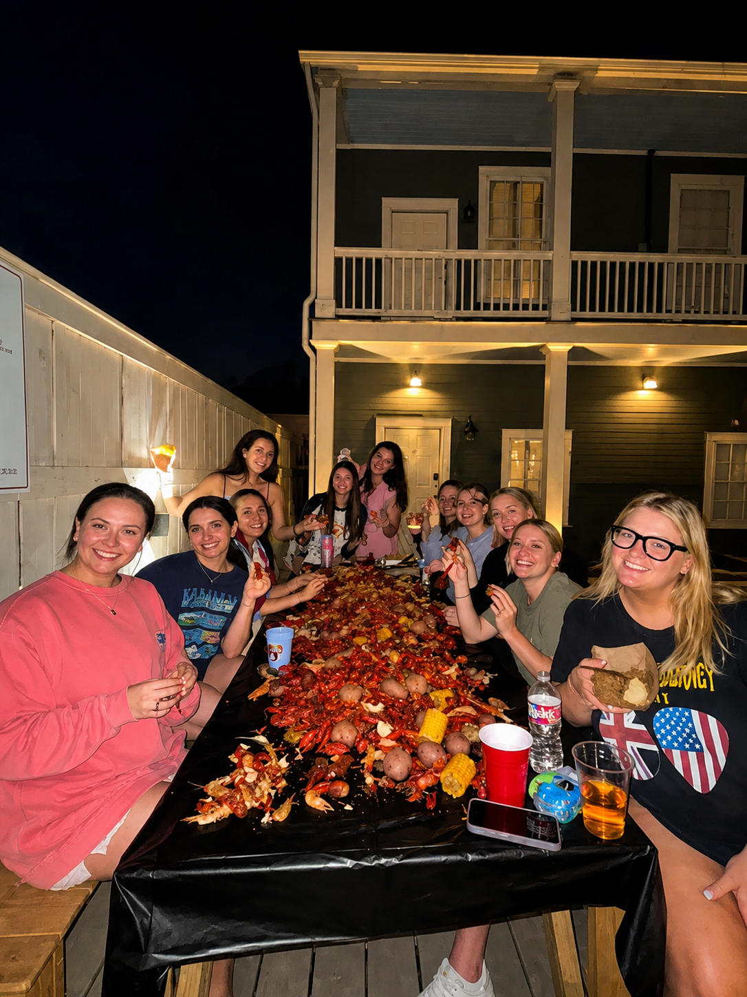 Group of people gathered around a table with food and drinks at night.