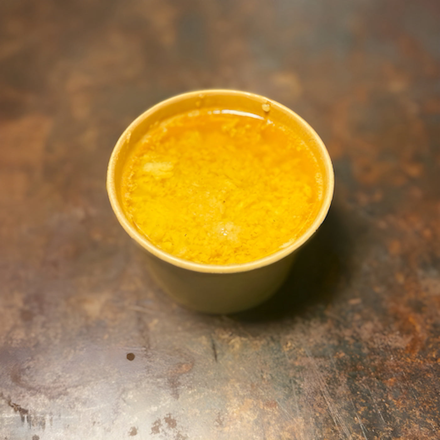 Yellow cup filled with a ya garlic butter seafood boil sauce made from scratch daily on a textured brown surface