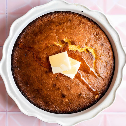 Made-from-scratch honey butter cornbread is Boil Baby Boil's signature offering in a ceramic dish with a pink tile background.