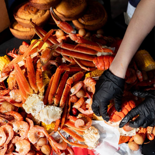 Seafood platter with lobster, shrimp, and corn on a table with a person wearing black gloves.