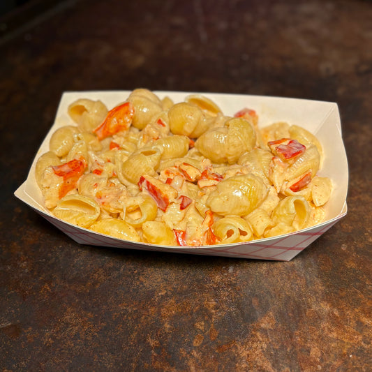 Macaroni and cheese with lobster in a paper container on a dark surface