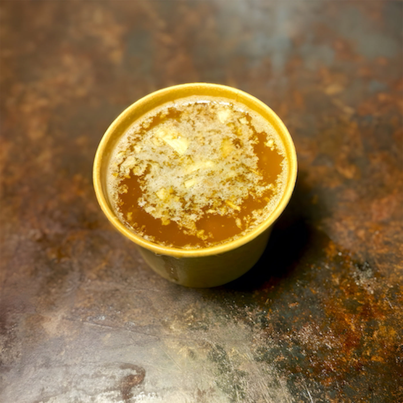 Yellow cup of Truff truffle butter seafood boil sauce on rustic metal surface at Cajun seafood boil in Los Angeles